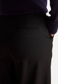Black pants featuring a smooth texture, tailored fit, and a back pocket with a subtle stitched detail. Complete with a dark purple knit top.