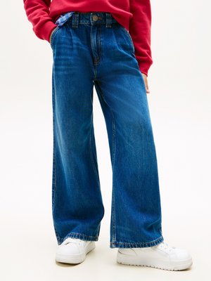 Široke modre jeans hlače z visokim pasom, ki imajo kontrastno šivanko in zapiranje na gumb, v kombinaciji z belimi supergami.