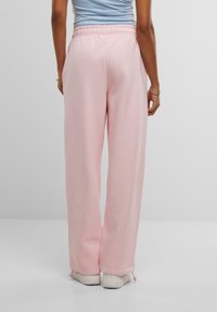 Lyserøde sweatpants med elastisk talje og løs pasform. Har snore ved ribkanterne og er parret med hvide sneakers.