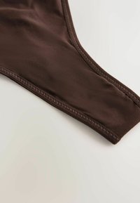 Tamsiai rudas bikini apatinis dalis, pasižymintis lygiu, tampri medžiaga su minimalistiniu dizainu ir sustiprintu siuvimu pakraščiuose.