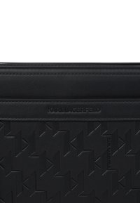 Geantă din piele neagră cu un design embosat ce prezintă modele KL interconectate. Textură netedă, cu o bandă orizontală cu logo și margini cusute.