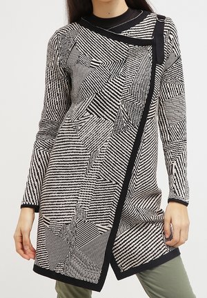 Vestito in maglia bianco e nero con motivi geometrici, colletto alto e frontale asimmetrico con un bordo nero a contrasto.