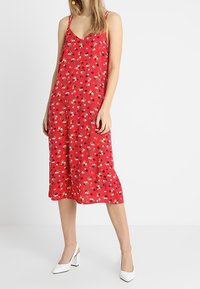 Robe d'été à imprimé floral rouge avec des bretelles fines et un décolleté en V, fabriquée en tissu léger, dotée d'une jupe mi-longue et d'une coupe décontractée.