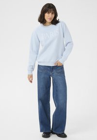 Ljust blå sweatshirt med "PARIS" tryckt i vitt. Kombinerad med vida blå jeans. Outfiten har en avslappnad stil och passform.