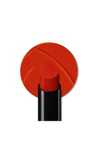 Rød leppestift med matt finish, pakket i et svart rør. Leppefargen har en avrundet spiss og vises mot en sirkulær rød bakgrunn.