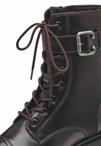 Stivale in pelle marrone con occhielli in metallo, lacci e una fibbia laterale. Caratterizzato da una finitura texturizzata e una suola robusta. Il design con lacci garantisce una vestibilità sicura.