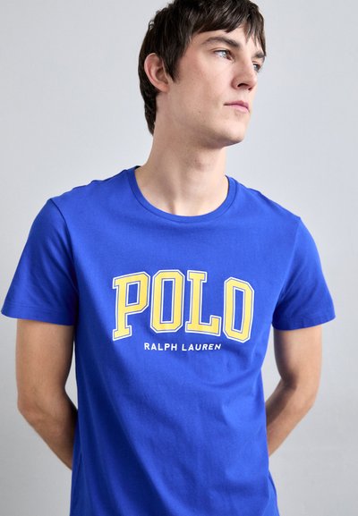 Camiseta de algodón azul con cuello redondo y mangas cortas, con el texto en negrita "POLO" en amarillo y "RALPH LAUREN" impreso debajo.