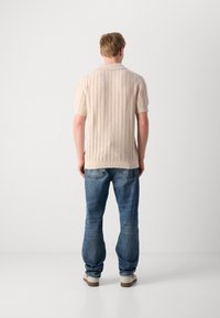 Knit polo shirt in light beige with short sleeves and ribbed collar, paired with relaxed-fit blue denim jeans and beige sneakers.