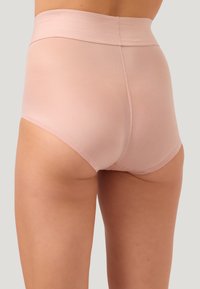 Vista posteriore di una persona che indossa lingerie seamless alta in vita di colore rosa chiaro su uno sfondo neutro.