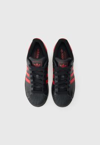 Czarne buty sportowe z trzema czerwonymi paskami, gumowym noskiem i czarnymi sznurowadłami. Wnętrze zdobi czerwone logo marki na wkładce.