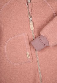 Myk rosa fleece-zipperhette med en stor frontlomme, ribbede mansjetter og et strukturert stoff. Har en beige glidelås og logotag.