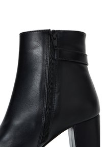 Bottine noire en cuir lisse, dotée d'une fermeture éclair sur le côté, d'un talon structuré et d'un design minimaliste avec un détail de sangle plate.