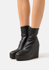 Melnu ādas augstas konusveida potītes zābaki ar rāvējslēdzēju, ar gludu tekstūru un noapaļotas pirkstu daļas dizainu. Platformas zole.