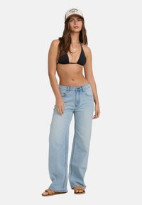 Ανοιχτό γαλάζιο παντελόνι με φαρδιά μπατζάκια και ψηλή μέση, συνοδευόμενο από μαύρο τριγωνικό μαγιό και μπεζ καπέλο. Πόδια σε επίπεδες σάντες.