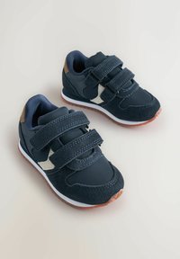 Mørkeblå sneakers til toddler med dobbel velcro-lukning, beige sideaccentuer, hvide mellemsåler og brune gummisåler mod en lys baggrund.