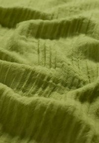 Tessuto verde testurizzato con superficie morbida e stropicciata, che mette in mostra un materiale leggero e traspirante in diverse sfumature di verde.