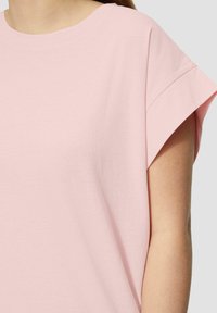 Helles rosa T-Shirt mit kurzen Ärmeln, aus weicher Baumwolle gefertigt, hat einen runden Ausschnitt und einen entspannten Schnitt mit hochgerollten Ärmeln.