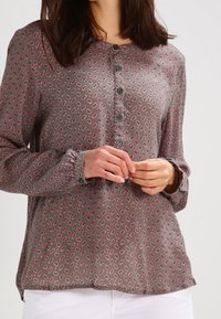 Blouse grise à manches longues avec un petit motif rose répétitif, boutons sur le devant et col rond. Tissu doux et coupe décontractée.