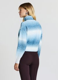 Maglione a collo alto azzurro chiaro con design ombre a gradiente, texture lavorata a maglia e polsini a costine, abbinato a pantaloni attillati marrone scuro.