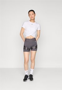 Valge lühikeste varrukatega särk, millel on seotud eesosa, hallid kõrge vöökohtadega lühikesed püksid "NIKE PRO" trükiga, valged sokid ja mustad spordijalatsid.