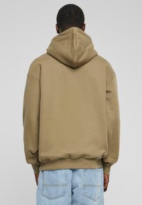 Felpa con cappuccio di colore verde oliva, realizzata in tessuto morbido. Caratterizzata da un fit rilassato, polsini e vita a coste, e un cappuccio spazioso.