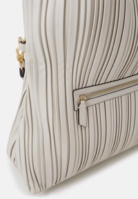 Geplooide beige leren handtas met een gouden ritssluiting, zwarte accenten en een gestructureerde vorm. Beschikt over een ritssluiting aan de buitenkant voor extra opbergruimte.