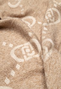 Manta de punto beige con una textura suave, que presenta un intrincado patrón crema de formas entrelazadas y puntos en todo su superficie.