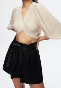 Lyse beige, stribet slå-om-top med pufærmer kombineret med en højtaljet sort nederdel med snøre i taljen og plisseret design.