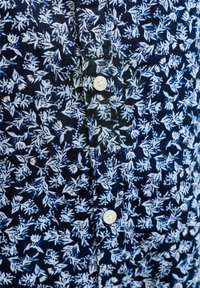 Μανδυά βαθύ μπλε με λευκό ανθικό μοτίβο που δείχνει μέρος του μπροστινού μέρους ενός πουκαμίσου με λευκά κουμπιά.