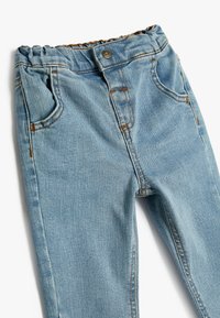 Jeans in denim azzurro chiaro con cintura elastica, tasche frontali e cuciture in contrasto marroni. Texture liscia, design aderente.
