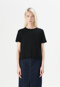 T-shirt noir à manches courtes avec un col rond, fabriqué en tissu doux. Coupé droit à l'ourlet, associé à une jupe en denim sombre.