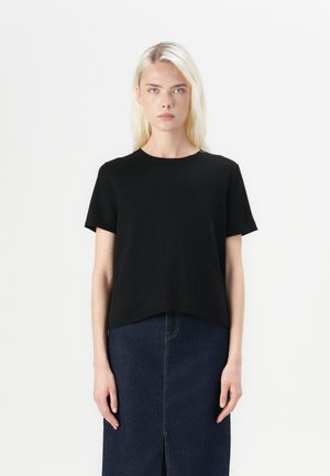 Svart kort erm t-skjorte med rund hals, laget av myk stoff. Klippet rett i kanten, paret med en mørk denimskjørt.