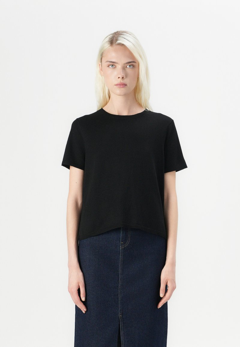 T-shirt noir à manches courtes avec un col rond, fabriqué en tissu doux. Coupé droit à l'ourlet, associé à une jupe en denim sombre.