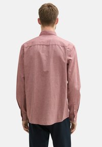 Camicia a maniche lunghe in tessuto rosso melangiato. Presenta un colletto classico, polsini con bottone e un orlo dritto con un leggero curvatura sul retro.