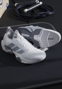 Coppia di scarpe sportive bianche e grigie su una superficie nera con una corda per saltare nera e grigia arrotolata sullo sfondo.