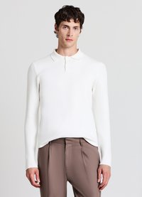 Weißes langärmliges Polo-Shirt mit Kragen, das ein strukturiertes Strickdesign aufweist, kombiniert mit braunen maßgeschneiderten Hosen.