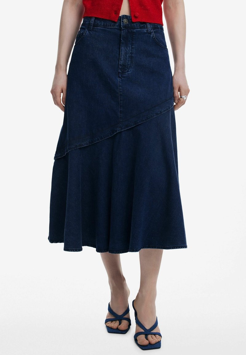 Denimhame, joka on korkea vyötärö ja tumman värinen, epäsymmetrinen helma ja virtaava siluetti. Viimeistelty tikkausviivoilla ja edessä olevalla napilla.