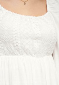 Vestido blanco con un corsé texturizado y patrones intrincados, y una cintura fruncida. La tela parece ligera con una falda fluida.