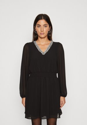 Abito nero con maniche lunghe, scollatura a V decorata con abbellimenti argentati, vita elastica e gonna fluente al ginocchio. Tessuto trasparente.