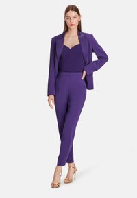 Purple tailored suit featuring a fitted blazer and matching trousers, with a textured bodysuit underneath and gold strappy heels.