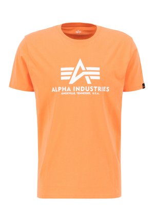 Oranžna bombažna majica s kratkimi rokavi, ki ima belo "Alpha Industries" logo in horizontalne črte v trikotni zasnovi na prsih.