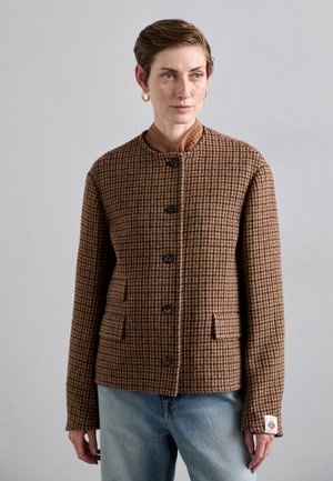Braun karierte Jacke mit Stehkragen, Knopfverschluss, zwei Vordertaschen und einem strukturierten Stoff. Getragen über hellblauen Jeans.