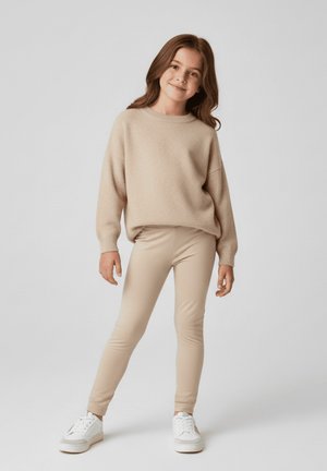 Beżowy sweter na drutach z opuszczanymi ramionami, połączony z jasnobeżowymi legginsami i białymi trampkami. Strój ma luźny krój i gładką fakturę.