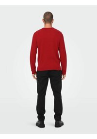 Czerwony sweter z dzianiny z okrągłym dekoltem, długimi rękawami i ściągaczami, w połączeniu z czarnymi spodniami i butami. Prosty design, standardowy krój.