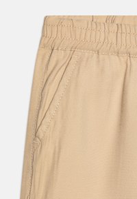 Pantalones de mezcla de algodón color beige con cinturilla elástica, bolsillo lateral y costuras visibles. Textura suave con un patrón de tejido ligeramente diagonal.