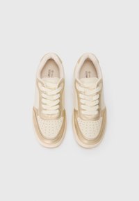 Cream and gold lace-up sneakers with perforated toe box, padded collar, and textured sole, shown from top view on white background.