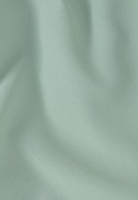 Tissu vert clair lisse avec des plis subtils et une texture douce légèrement brillante.