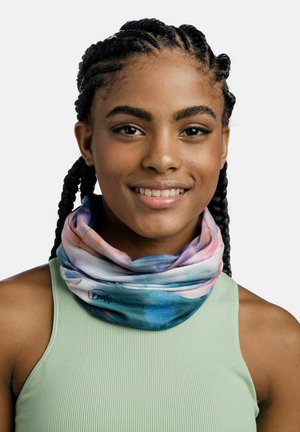 Junge Frau mit geflochtenem Haar lächelt, trägt einen pastellfarbenen Batik-Halsschlauch und ein hellgrünes ärmelloses geripptes Oberteil vor weißem Hintergrund.