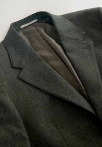 Blazer de lana gris con solapa de muesca, corte entallado y forro oscuro con estampado, que muestra una textura suave y un diseño estructurado.