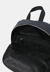 Sac à dos en nylon noir avec une fermeture éclair, doté d'un intérieur spacieux, de plusieurs poches et d'un logo discret sur la doublure.